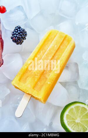 Detox, healthy yellow smoothie popsicles over the ice with slice lime and berries, flat lay Stock Photo