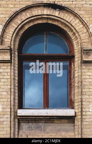 Vintage arched window in the wall of yellow brick. Black glass in a maroon dark red wooden frame. The concept of antique vintage Stock Photo