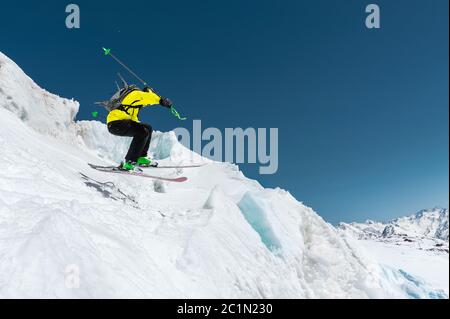 A skier in full sports equipment jumps into the abyss from the top of the glacier against the background of the blue sky and the Stock Photo