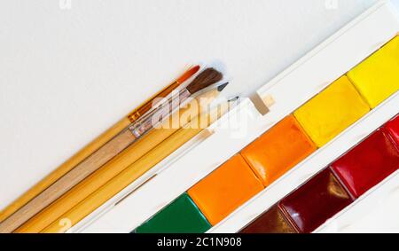 brushes and pencils next to watercolors on white paper top view copy space Stock Photo