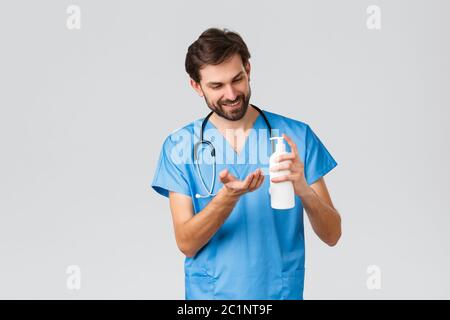 Healthcare workers, pandemic and coronavirus outbreak concept. Handsome doctor or nurse in scrubs, apply hand sanitizer or soap to clean hands during Stock Photo