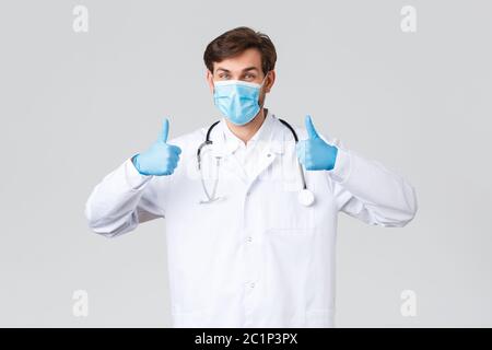 Hospital, healthcare workers, covid-19 treatment concept. Supportive optimistic doctor in scrubs, medical mask and rubber gloves, thumb-up in approval Stock Photo