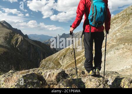 The body of man with a backpack and trekking poles stands on top of a rock against the background rocky valley high in the mount Stock Photo