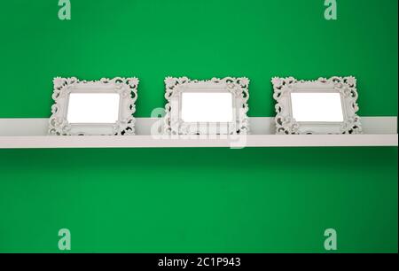 three white empty photo frames on a green wall and wooden shelf, isolated, space for text or photo Stock Photo