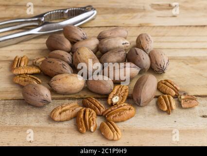 Pecan nuts on rustic wooden table, whole and peeled with nut cracker in background - selective focus Stock Photo