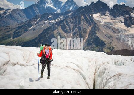 Female mountaineer enjoying the beauty of the glacier walks on the glacier in the crampon and sunglasses. Against the backdrop o Stock Photo