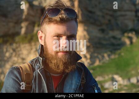 Close-up portrait of a bearded stylish traveler in a cap against epic rocks. Time to travel concept Stock Photo