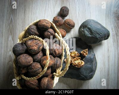 The whole walnuts are  into a wicker basket next to Walnuts broken on the stone on wooden table. Organic Ripe walnut kernels. Close up. Top view. Heal Stock Photo