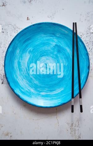 Turquoise hand painted ceramic serving plate with wooden chopsticks on side Stock Photo