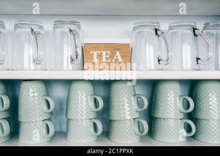 tea cups and coffee mugs on a kitchen shelf with a tea box Rack focus. Close up. Stock Photo
