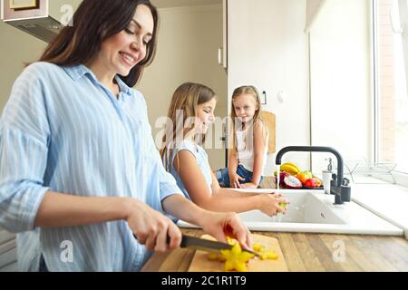 Beautiful little girls with they mother in the kitchen preparing a fruit salad Stock Photo