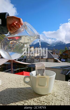Closeup Hand Pouring Hot Water into the Portable Drip Coffee Bag with Caucasus Mountains View in Background Stock Photo