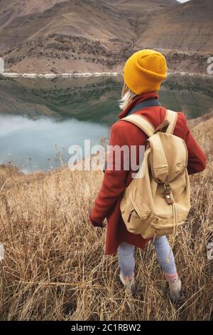 A portrait from the back of a girl traveler on the background of a lake in the mountains in autumn or early spring. Travel conce Stock Photo