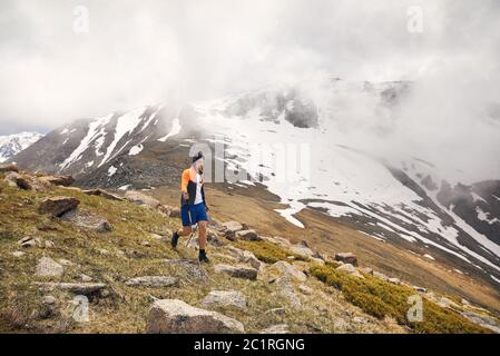 Tourist with trekking poles is walking in the mountain valley in foggy day. Concept of outdoor activity lifestyle. Stock Photo
