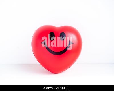 Red heart. Close-up happy smiley face on big red heart ball on white clean table on white background.