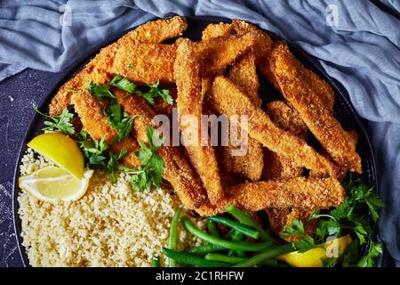 close-up of green beans with fish sticks, fish fillet fingers breaded and deep-fried served on a black plate with couscous on a concrete table, landsc Stock Photo