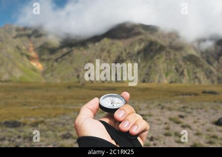 Viewpoint shot. A first-person view of a man's hand holds a compass against the background of an epic landscape with cliffs hill Stock Photo