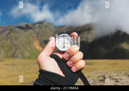 Viewpoint shot. A first-person view of a man's hand holds a compass against the background of an epic landscape with cliffs hill Stock Photo