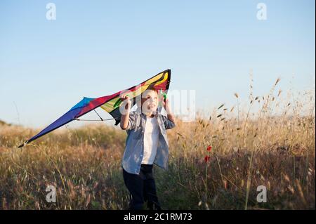 worried little boy with kite looking up in dry yellow summer field with blue sky on background Stock Photo