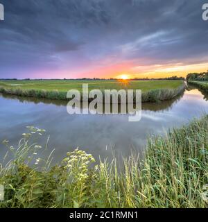 Wide angle landscape over river bend at sunset in flat agricultural landscape in Groningen the Netherlands Stock Photo