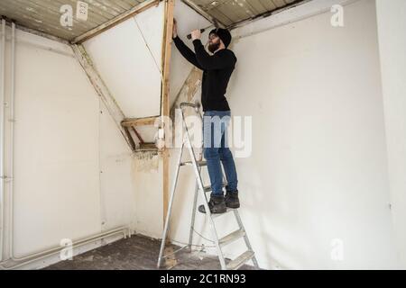 Handyman standing on a ladder and renovating a home, using tools like a hammer Stock Photo