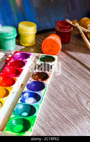 Tempera paints on the table in a workshop, selective focus, Set of watercolor paints, brushes for painting and palette Stock Photo