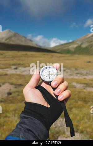 Viewpoint shot. A first-person view of a man's hand holds a compass against the background of an epic landscape with cliffs hill Stock Photo