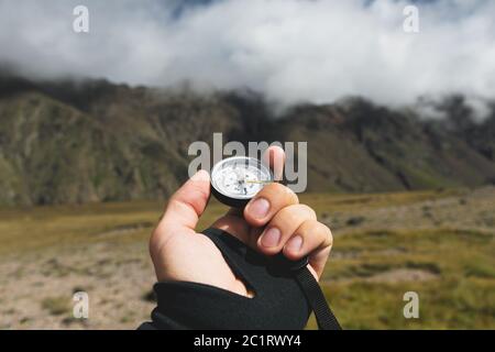 Viewpoint shot. A first-person view of a man's hand holds a compass against the background of an epic landscape with cliffs hill Stock Photo