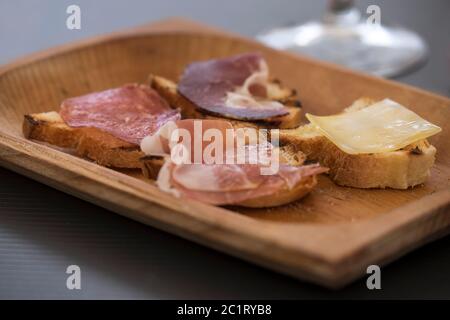 Wooden bowl on a table with Italian bruscetta with salami, meat and cheese. Selective focus Stock Photo