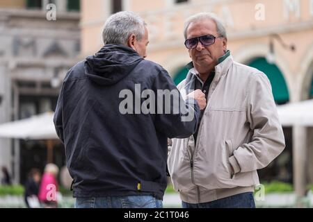 TwoItalian men talk and gesture to each other on the square Piazza del Popolo in Ascoli Piceno, Italy Stock Photo