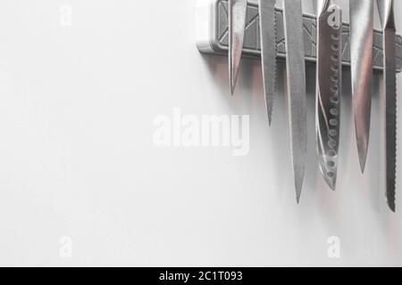 Knives on magnetic wall support in a kitchen on white wall, space for text Stock Photo