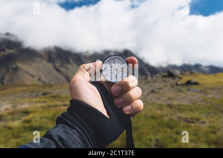Viewpoint shot. A first-person view of a man's hand holds a compass against the background of an epic landscape with cliffs hill Stock Photo
