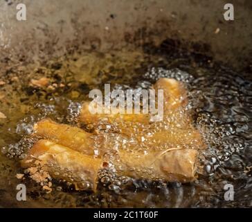 Close up shot of deep fried spring rolls being fried in hot oil in a large kitchen wok. The spring rolls bubble and turn golden brown in the hot oil Stock Photo