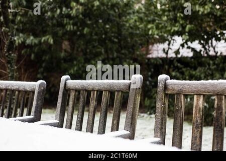 Wooden cozy garden chairs covered in snow in a backyard garden. Stock Photo