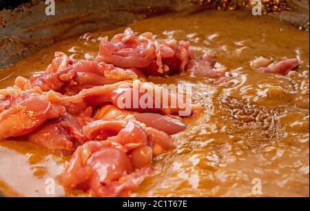 Close up shot of chicken meat being added to a creamy Thai red curry dish.  The fresh meat has just been added to the wok and has yet to be stirred in. Stock Photo
