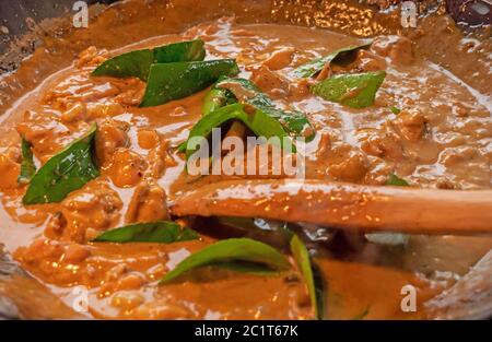 A chef stirs a creamy sauce of a Thai red chicken curry. The creamy coconut sauce cooks the vegetables and meat in the hot wok. Stock Photo