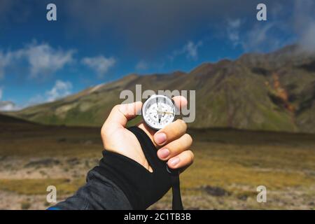 Viewpoint shot. A first-person view of a man's hand holds a compass against the background of an epic landscape with cliffs hill Stock Photo