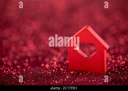 Small house with heart shape on red glitter background Stock Photo