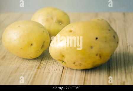 Three Raw potatoes on a wooden cutting board. Fresh organic potato. Stock Photo