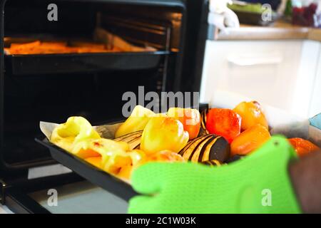 Close up shot of roast pepper and eggplant in a tray. A man is holding it in his hands wearing oven gloves Stock Photo