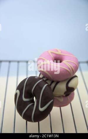A stack of sweet donuts of different colors and flavors of strawberry, dark and white chocolate on a grill and with copy space Stock Photo