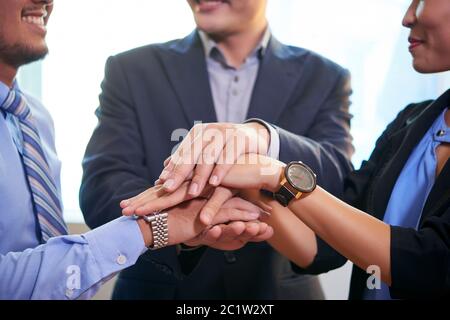 Team of three Asian business people joining their hands making unity gesture, horizontal shot Stock Photo