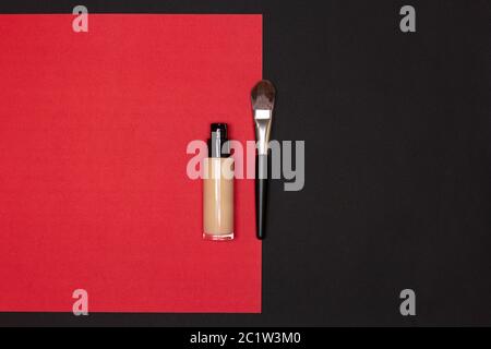 Make-up foundation bottle with flat makeup brush on red and black background. Top view. Copy space Stock Photo