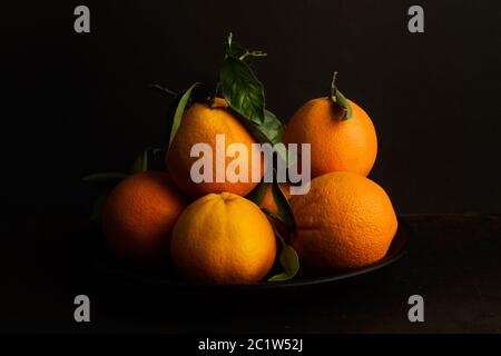 Heap of oranges with green leaves on a black plate and on a dark background Stock Photo
