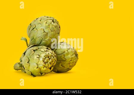 Three artichokes in a pile on a yellow background Stock Photo