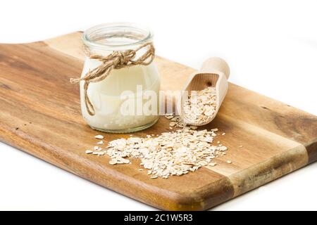 A jar of milk and oat flakes in a wooden scoop on a wooden kitchen board Stock Photo