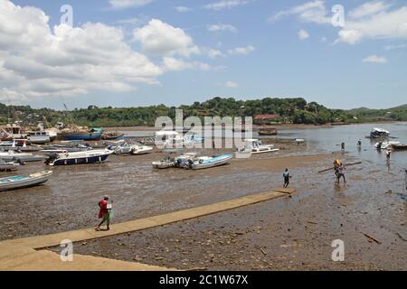 Beached boats and man carrying log in Andoany Harbour or Hell-Ville Harbour, Nosy Be, Madagascar. Stock Photo