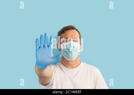Man standing on a light blue background with medical gloves and mask and doing stop gesture Stock Photo