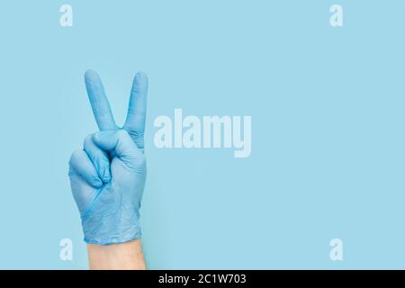 Man hand with medical gloves doing fingers victory gesture on a light blue background Stock Photo