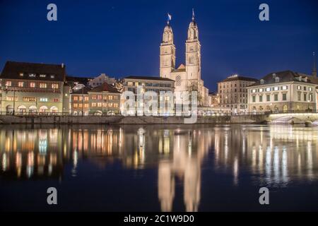 ZURICH, SWITZERLAND - 17TH APRIL 2018: The Grossmünster Church and Limmatquai street in Zurich from across the Limmat River at night. Stock Photo